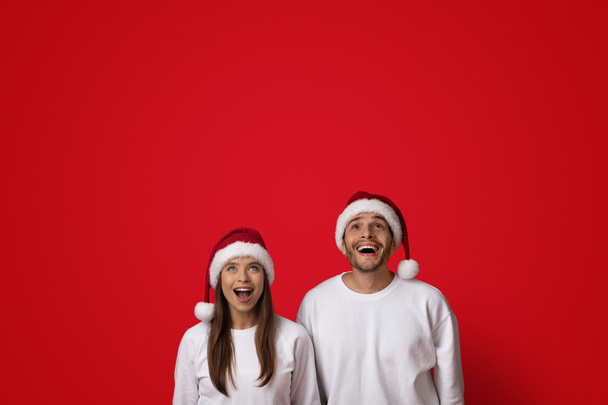 Harika bir teklif. Heyecanlı Noel Baba Şapkalı Genç Çift Şaşkınlıkla Yukarı Bakıyor - Fotoğraf, Görsel