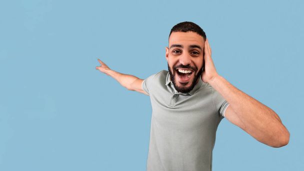 Chico árabe sorprendido agarrando su cabeza y apuntando al espacio en blanco con la boca abierta, ofreciendo grandes descuentos, fondo azul - Foto, imagen