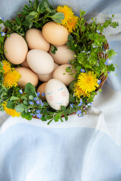 イースターの卵を描いた木製のバスケットに美しい春の花束、かわいい顔をした卵。イースター休暇のためのカラフルなグリーティングカード - 写真・画像