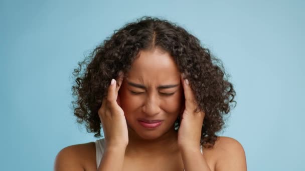 African Woman Suffering From Headache Massaging Temples Over Blue Background - Imágenes, Vídeo