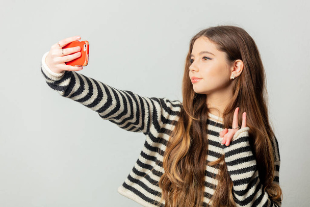Krásná dívka v pruhovaném svetru vzít selfie na bílém pozadí - Fotografie, Obrázek