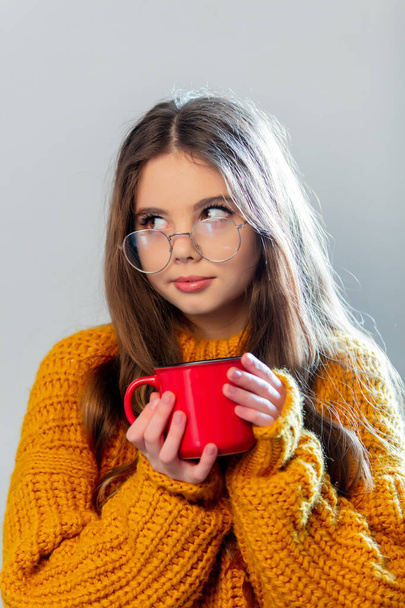 Beautiful girl in glasses and yellow sweater with red mug on white background - Fotoğraf, Görsel