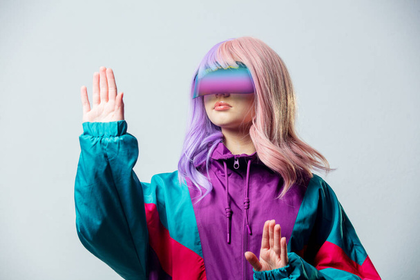 Teen girl in VR glasses and purple 80s tracksuit on gray background - Foto, Imagen