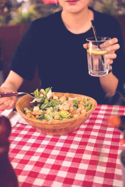 Porträt einer attraktiven kaukasischen lächelnden Frau, die Salat isst, sich auf Hand und Gabel konzentriert. - Foto, Bild