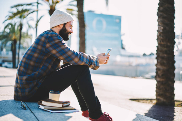 Middle Eastern student chatting with followers from social network via app on mobile phone, millennial hipster guy typing text message via cellphone technology connect to 4g wireless in roaming - Fotoğraf, Görsel