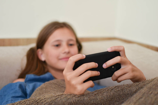 girl lies on the couch with the phone. teenager girl playing on the smartphone. children's gambling addiction. online learning - Foto, imagen