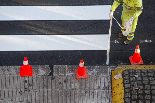 Trabajador quitando cinta adhesiva después de pintar un cruce de cebra en una carretera de la ciudad - Foto, Imagen