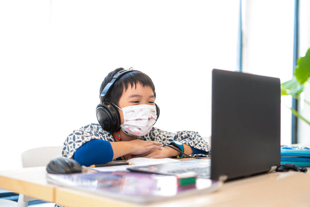 Aasialainen poika onnellinen käyttämällä kannettavaa tietokonetta opiskelee verkossa kotona kotona karanteeniepidemian aikana, chat-ystävä tai opettaja tai vanhempi tietokoneen kautta. kotikoulu, verkko-opiskelu, verkko-oppiminen, koronavirus tai teknologiakonsepti - Valokuva, kuva