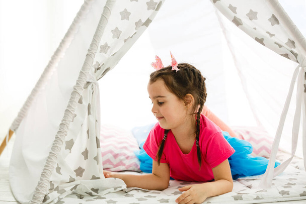 Enjoying great story. Cute little girl on the floor in tent - Фото, изображение