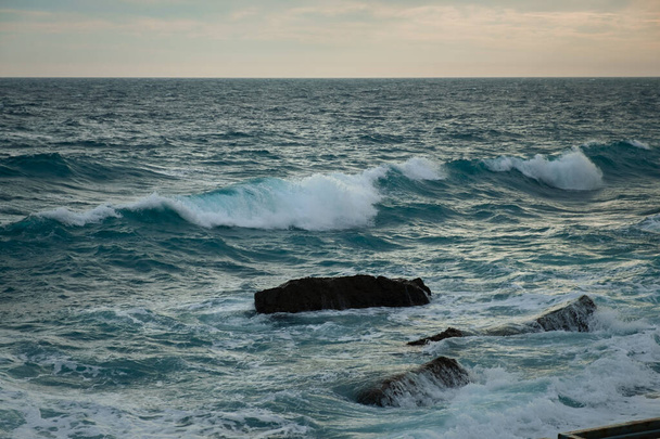 Turquoise sea stone beach, breaking waves on a cloudy spring day. Beautiful sea background. The concept of summer, vacation, travel. The purest clear sea water, large stones on the beach close-up - Foto, imagen