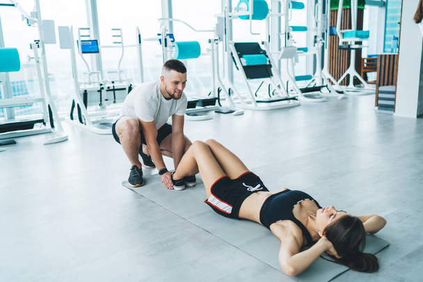 Happy active sporty fit couple doing abdominal exercises on floor covered with mat near gym equipment in light modern gym - Fotoğraf, Görsel