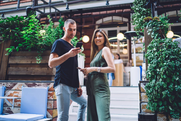 Half length portrait of millennial couple in love using cellphones at city street, Asian woman smiling at camera while boyfriend browsing travel website on modern smartphone technology connect to 4g - Foto, Bild