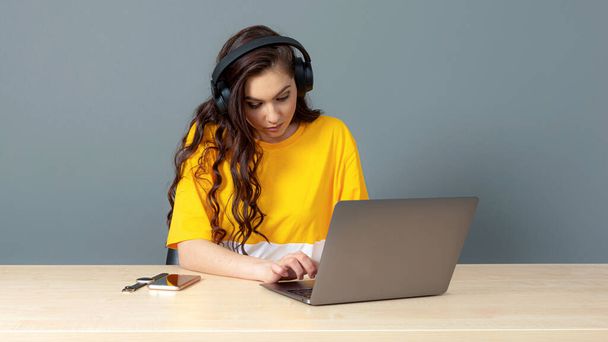 de student zit met een headset achter de computer en kijkt en luistert online naar video-tutorials - Foto, afbeelding