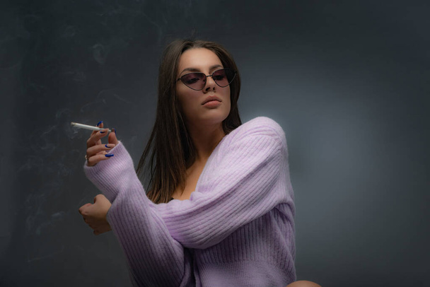 Atractiva y hermosa chica caliente está posando con el cigarrillo en la mano mientras lo fuma - Foto, imagen