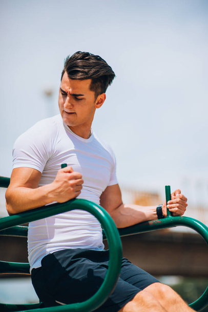 Active and young man doing abdominal workout on chin up bar - Fotó, kép
