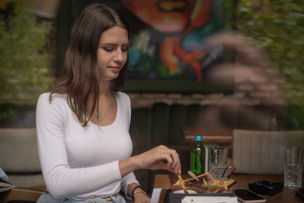 Muchacha atractiva está tomando papas fritas antes de comer en el bar del almuerzo - Foto, imagen