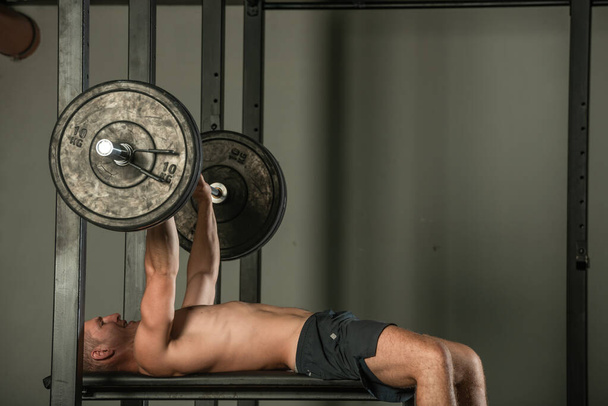 Atletyczny kulturysta mięśni robi na ławce wyciskanie treningu w pomieszczeniach w nowoczesnej siłowni. - Zdjęcie, obraz