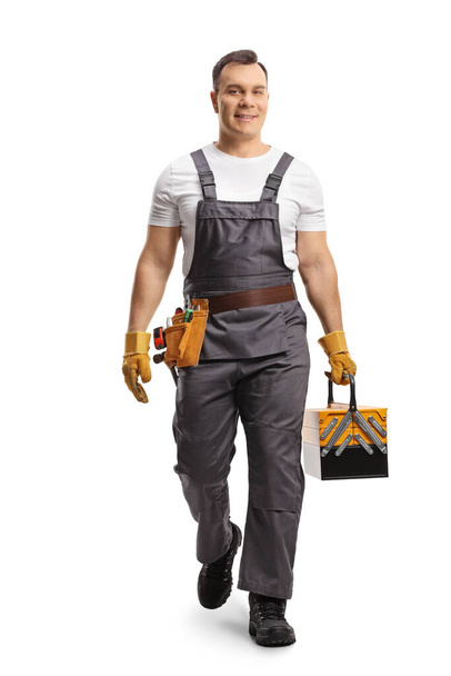 Retrato completo de un reparador en uniforme que lleva una caja de herramientas y camina hacia la cámara aislada sobre fondo blanco - Foto, imagen
