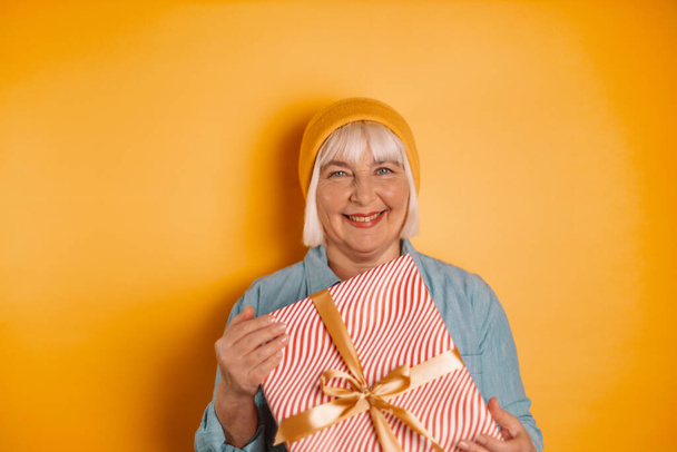 Retrato de atractivas y divertidas manos de mujer de los años 40 y 50 sosteniendo una caja de regalo sobre un fondo de color naranja brillante. Vacaciones de Navidad, presente, concepto de felicidad - Foto, Imagen