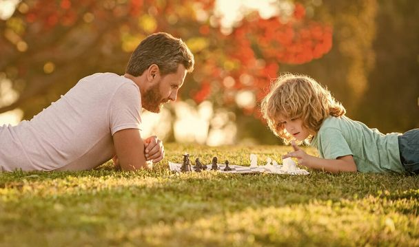 šťastná rodina tatínek a syn dítě hrát šachy na zelené trávě v parku venku, hrát šachy - Fotografie, Obrázek