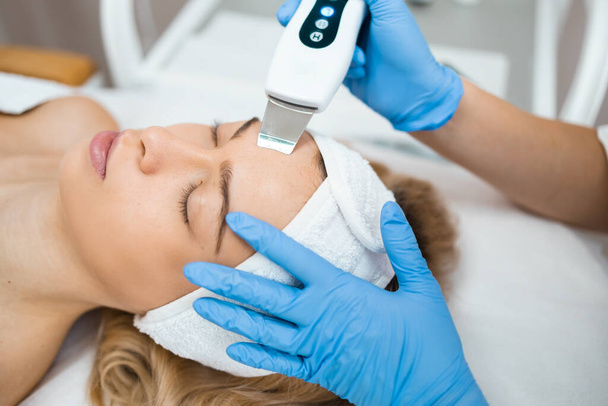 El primer plano de la mujer relajada recibe la limpieza facial ultrasónica de las manos de un cosmetólogo profesional. Pelar la piel de la cara en un salón de belleza - Foto, Imagen