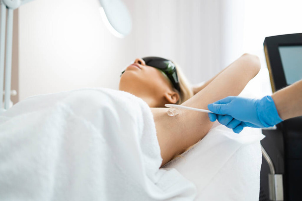 Applying hair removal gel under the arms. Woman at a laser epilation session with a modern laser in a beauty studio - Photo, Image