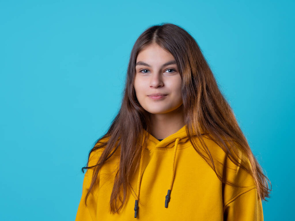 A beautiful young brunette in a yellow oversize hoodie, a positive student - 写真・画像