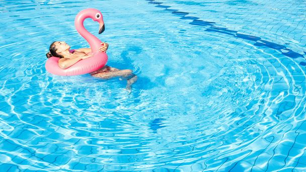 Mulher à beira da piscina. Menina sexy feliz em biquíni maiô com flamingo rosa flutuar em água azul. Viagem de luxo estilo de vida - Foto, Imagem