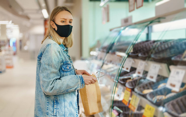 Woman in medical mask chooses bread at grocery store. - Foto, Imagem