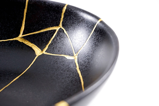 Isolated black Japanese kintsugi bowl, antique pottery restored with gold cracks. Traditional gold fixing method. - Фото, изображение