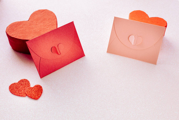 περιστασιακοί διακοσμητικοί κόκκινοι και ροζ φάκελοι με κλείσιμο που συμβολίζει την αγάπη σε ένα ασημί λαμπερό φόντο, κόκκινο φυσικό κουτί δώρου σε σχήμα καρδιάς για ένα αγαπημένο πρόσωπο Ένα μέρος για ευχές ή μια εξομολόγηση αγάπης  - Φωτογραφία, εικόνα
