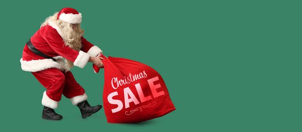 Santa Claus with heavy bag on green background. Christmas sale - Фото, изображение