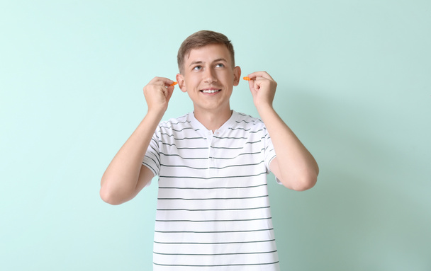 Handsome young man inserting earplugs on blue background - Fotó, kép