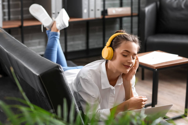 Mooie jonge vrouw met laptop die thuis naar muziek luistert - Foto, afbeelding