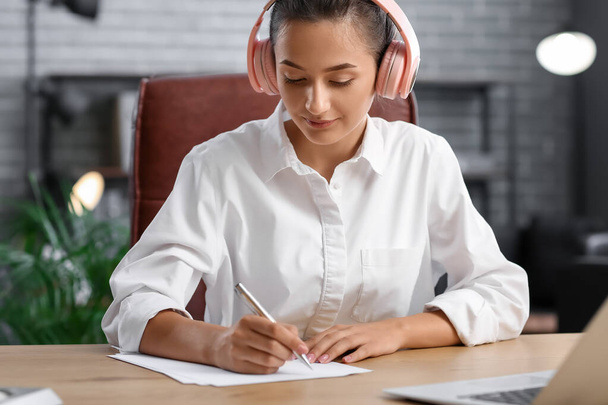 Mooie jonge vrouw luisteren naar muziek tijdens het werk in het kantoor - Foto, afbeelding