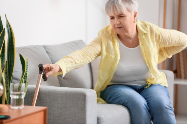 Senior woman with back pain taking walking stick at home - Foto, immagini