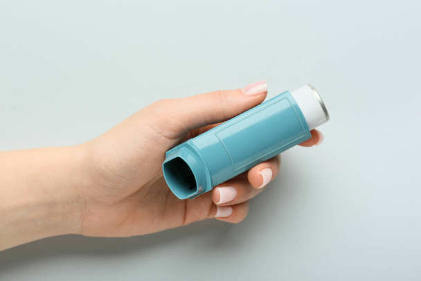 Mano femenina con inhalador de asma moderno sobre fondo gris - Foto, imagen