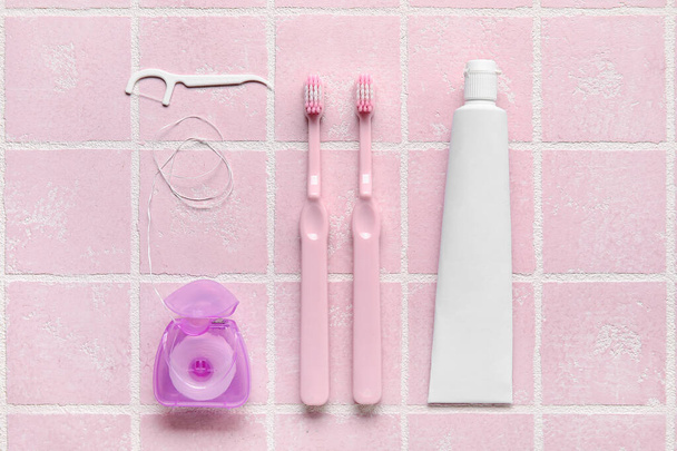 Tandflos met tandenstokers, borstels en plakken op roze tegelondergrond - Foto, afbeelding