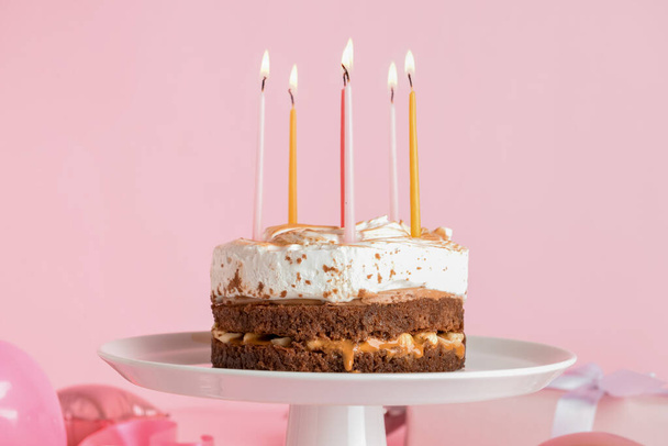 Stand with tasty birthday cake and burning candles on pink background - Фото, изображение