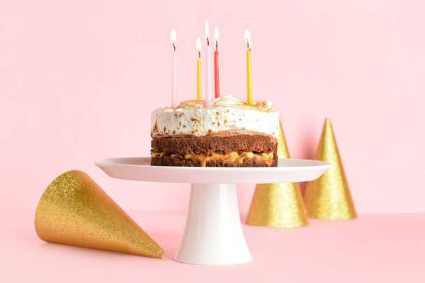 Lezzetli doğum günü pastası ve pembe arka planda parti şapkalarıyla durun. - Fotoğraf, Görsel