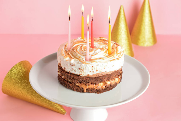 Stand with tasty birthday cake and party hats on pink background - Zdjęcie, obraz