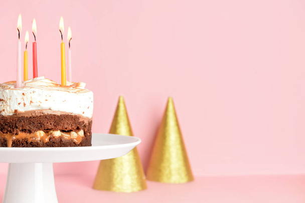 Stand with tasty birthday cake and party hats on pink background, closeup - Foto, Imagem