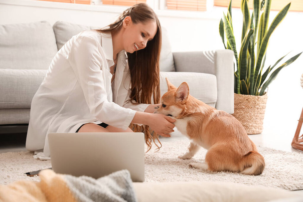 Young woman with cute Corgi dog sitting on floor at home - Foto, Imagen