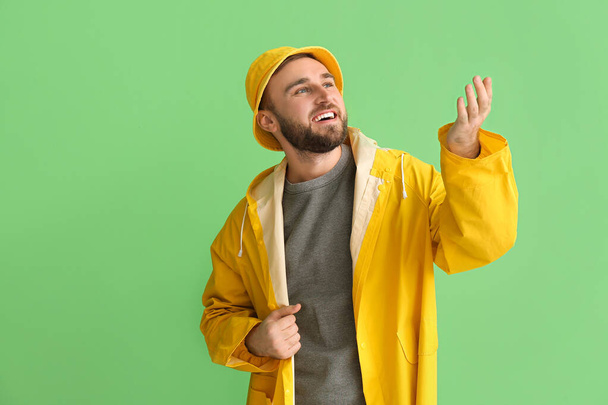 Young man in stylish raincoat showing something on color background - Photo, Image