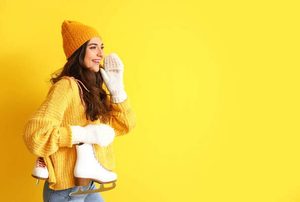 Pretty young woman in winter clothes and with ice skates on color background - Fotó, kép