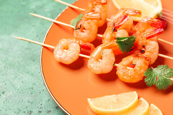 Plate with grilled shrimp skewers and lemon on green background, closeup - Фото, изображение