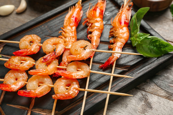 Board with grilled shrimp skewers on wooden background, closeup - Photo, Image
