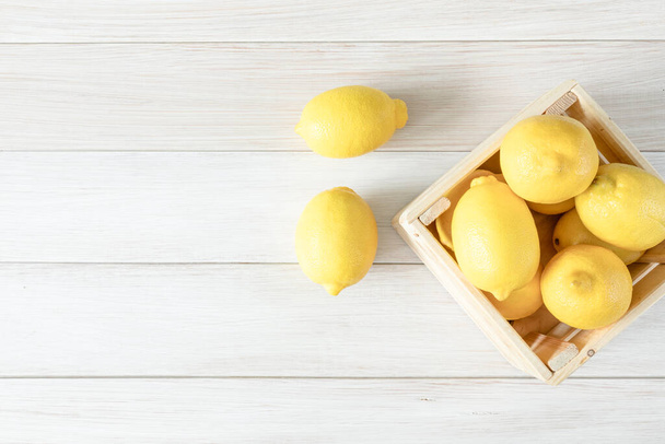 Ripe lemons in a wooden box. Fresh lemons on a white wooden background. Top view. Ripe and tasty citrus fruit. Copy space for text - Foto, imagen