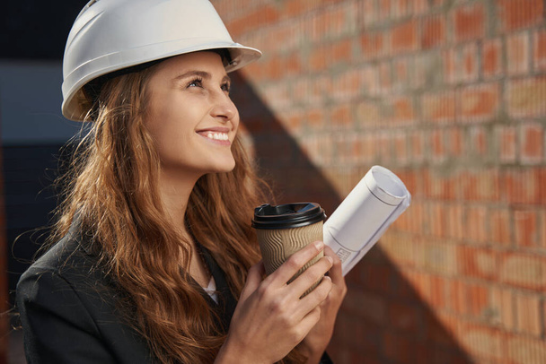 Happy woman engineer with coffee looking up - Фото, зображення