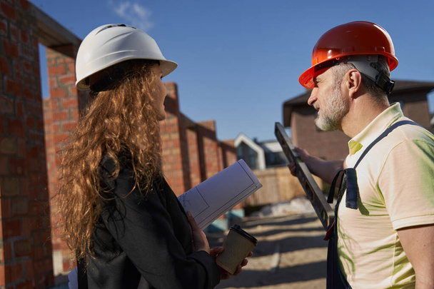Housebuilder looking at female civil engineer and pointing with level - Foto, afbeelding